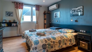 Un dormitorio con cama, mesita de noche, estantería y ventana con cortinas.