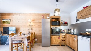 Een moderne keuken met houten kastjes, roestvrijstalen apparatuur en een eethoek met een tafel voor vier personen.
