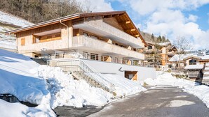 Een houten chalet met een balkon, omringd door sneeuw en een heldere lucht.