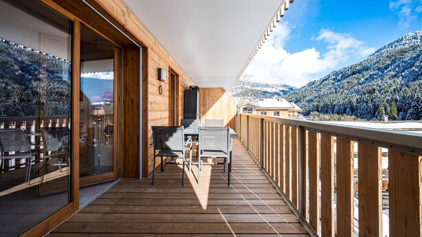 Een houten terras met een tafel en stoelen, met uitzicht op een besneeuwd berglandschap.