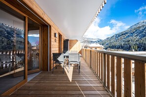Een houten terras met een tafel en stoelen, met uitzicht op een besneeuwd berglandschap.