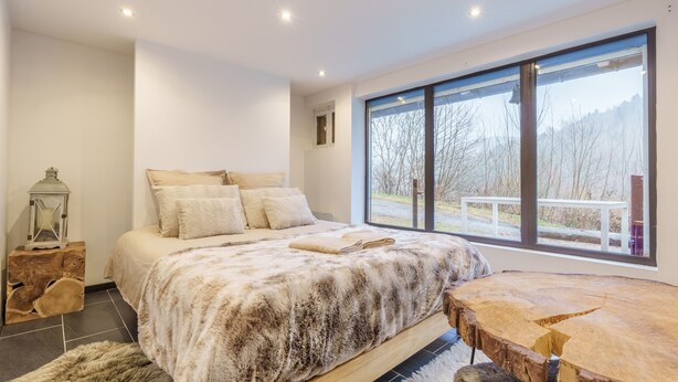 Une chambre moderne avec un grand lit, une table de chevet en bois et une vue sur un paysage enneigé par une grande fenêtre.