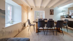 Un coin repas avec une table et des chaises en bois, une fenêtre donnant sur un paysage agréable et un espace cuisine avec une lampe.
