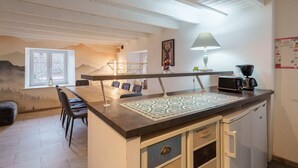 Une cuisine avec un îlot central en bois, un coin repas avec des chaises, un réfrigérateur et une fenêtre donnant sur des arbres.