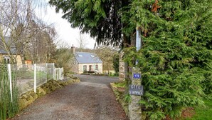 A gravel driveway leading to a stone house with a sign indicating 'GITE LE NYMPHEA'. - Le Lotus - 1000 m² de jardin (Putanges-le-Lac)