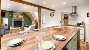 A modern kitchen with a wooden island, built-in stove, and a stone fireplace. - Le Lotus - 1000 m² de jardin (Putanges-le-Lac)