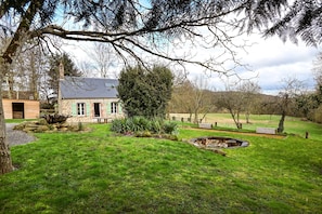 A stone house with a green roof, surrounded by a well-maintained lawn and a small pond. - Le Lotus - 1000 m² de jardin (Putanges-le-Lac)
