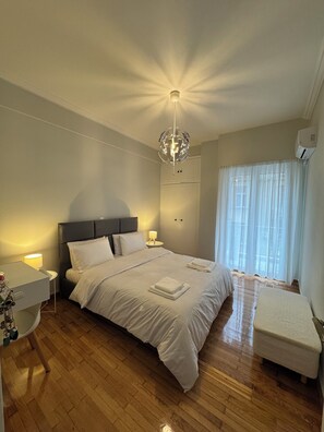 A bedroom with a bed, bedside tables, a nightstand, a bench, a chandelier, and a window with curtains. - Cozy bright 1 bedroom in cental athens enjoy a sun filled (Athina)