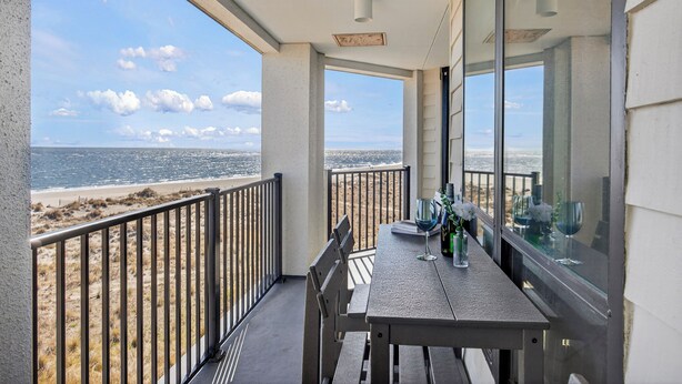 Un balcon avec vue sur la plage et l’océan, une table avec des chaises et une porte vitrée.