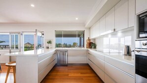 A modern kitchen with white cabinetry, a stainless steel dishwasher, and a large window offering a view of the outdoors.