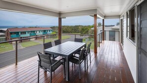 A balcony with a wooden floor, a table with chairs, and a view of houses and greenery.