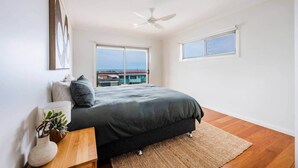 A bedroom with a bed, a ceiling fan, and a view of buildings through large windows.