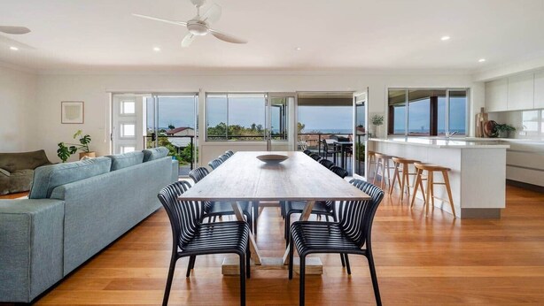 A modern living space with a dining area, kitchen, and large windows offering a view of the sea.