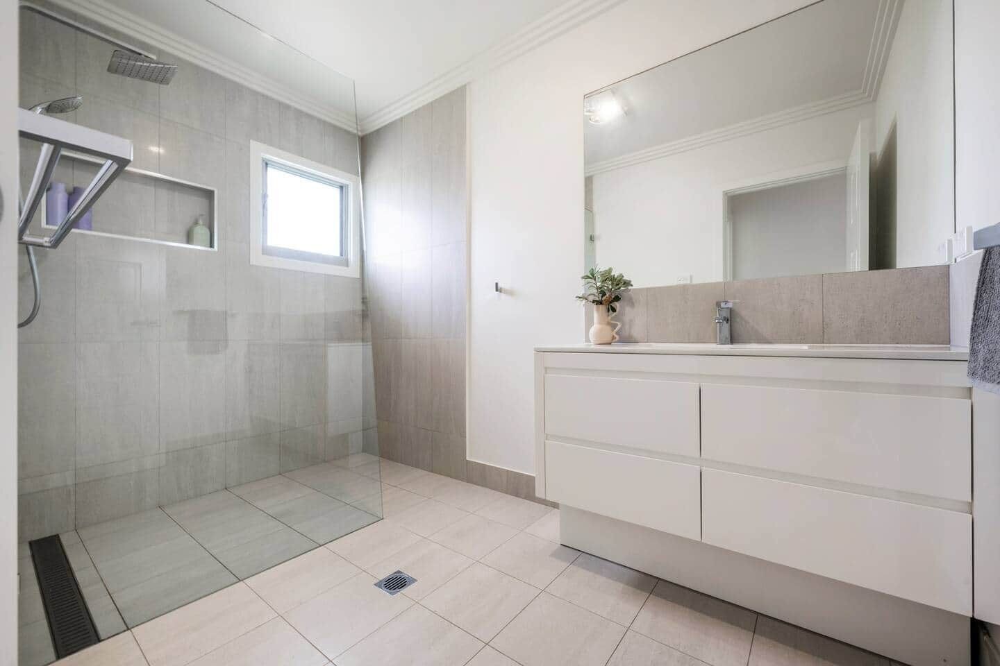 A modern bathroom with a glass shower enclosure, a large mirror, and a vanity with multiple drawers.