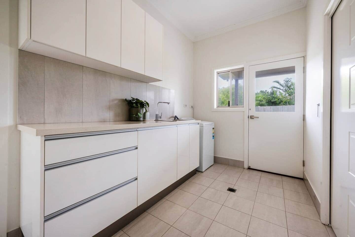 Une cuisine moderne avec des meubles blancs, un four encastré et une fenêtre donnant sur un paysage verdoyant.