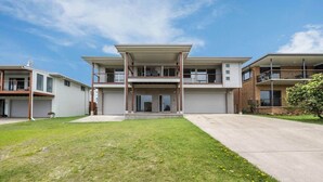 A modern two-story residential building with a flat roof, large windows, and a covered front porch.