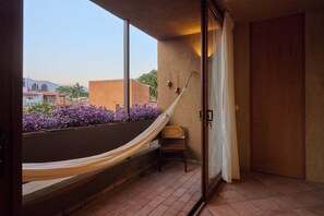Un balcón con una hamaca, una silla y vistas a edificios y flores.