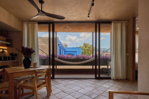 A room with a dining table, chairs, a ceiling fan, and a view of a blue building through large glass doors. - Casona Xochimilco - Jalatlaco (Oaxaca de Juárez)