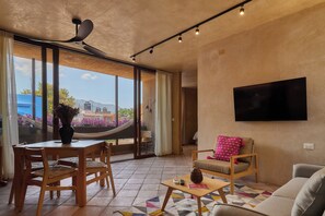 A modern living room with a dining area, a sofa, a TV mounted on the wall, and a view of the outdoors. - Casona Xochimilco - Jalatlaco (Oaxaca de Juárez)