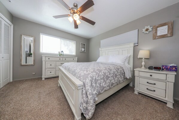 A bedroom with a bed, a nightstand, a dresser, a ceiling fan, and a window.