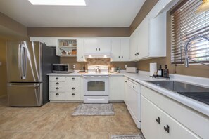A modern kitchen with stainless steel appliances, white cabinetry, and a large window with blinds.