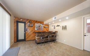 A hallway with a wooden wall, a door, a bar area with stools, and a tiled floor.