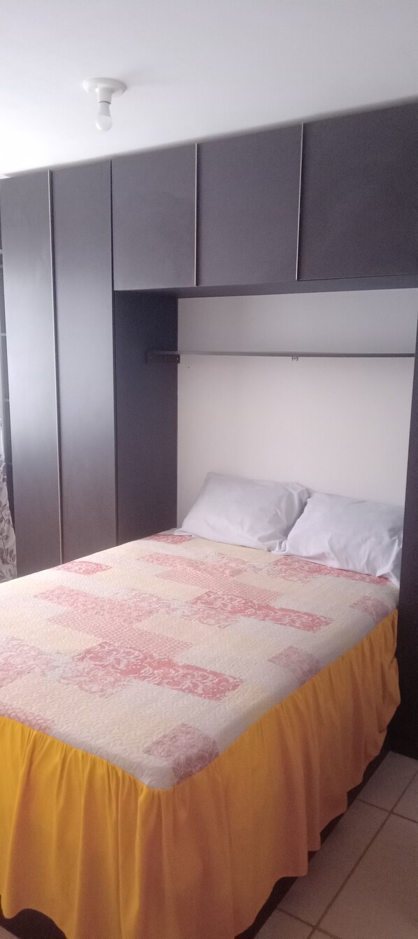 A bed with a patterned bedspread, a headboard, and a yellow skirted bed base.