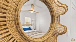 A bedroom with a bed, a ceiling fan, and a mirror with a woven frame.