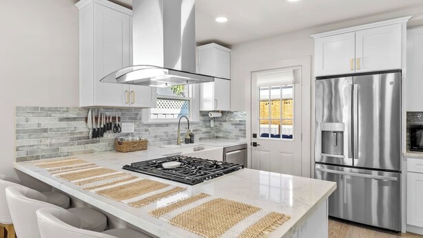 A modern kitchen with white cabinets, a stainless steel refrigerator, and a central island with stools.