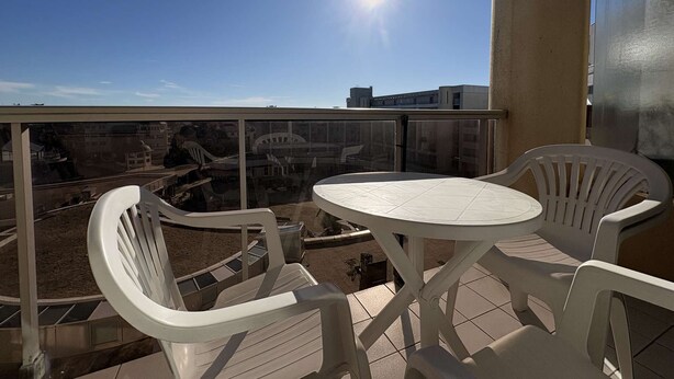 Ein Balkon mit rundem Tisch und zwei Stühlen, mit Blick auf eine Stadtlandschaft mit Gebäuden und einer Brücke.