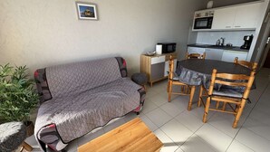 Ein kompakter Wohnbereich mit Sofa, Esstisch und Stühlen, einer kleinen Küchenzeile und einem Blumentopf.