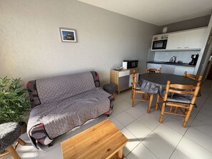 Ein kompakter Wohnbereich mit Sofa, Esstisch und Stühlen, einer kleinen Küchenzeile und einem Blumentopf.