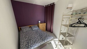 Ein kleines, ordentlich eingerichtetes Schlafzimmer mit Bett, Kleiderschrank und Kleiderständer.