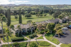 A residential area with a golf course, palm trees, and a building with a tiled roof. - Royal Turtle Palms: Luxe 4BR Turtle Bay Condo, Sleeps 12 (Kahuku)