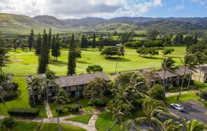 A golf course with a building in the foreground, surrounded by greenery and hills in the background. - Royal Turtle Palms: Luxe 4BR Turtle Bay Condo, Sleeps 12 (Kahuku)