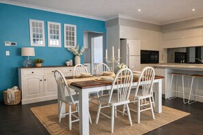 Una cocina moderna con armarios blancos, una zona de comedor con mesa de madera y sillas blancas, y una pared de acento azul.