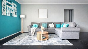 A modern living room with a grey sectional sofa, a round wooden coffee table, and a teal accent wall. - Coastal retreat 2km from the beach (Golden Bay)