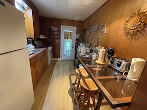 A kitchen with wooden cabinets, a refrigerator, a stove, and a sink. There is a wooden island with stools, a toaster, and a knife block. - Port Elgin Shimmering Shores Cottage Rental (Port Elgin)