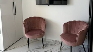 Een moderne kamer met een flatscreen televisie aan de muur, twee roze fauteuils, een witte kledingkast en een marmeren vloer.