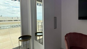 Een moderne kamer met een groot raam, een garderobe, een klein rond tafeltje en een roze stoel.