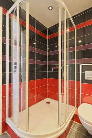 Un espace douche doté d’une porte en verre, de murs carrelés en rouge et noir, et de toilettes blanches.