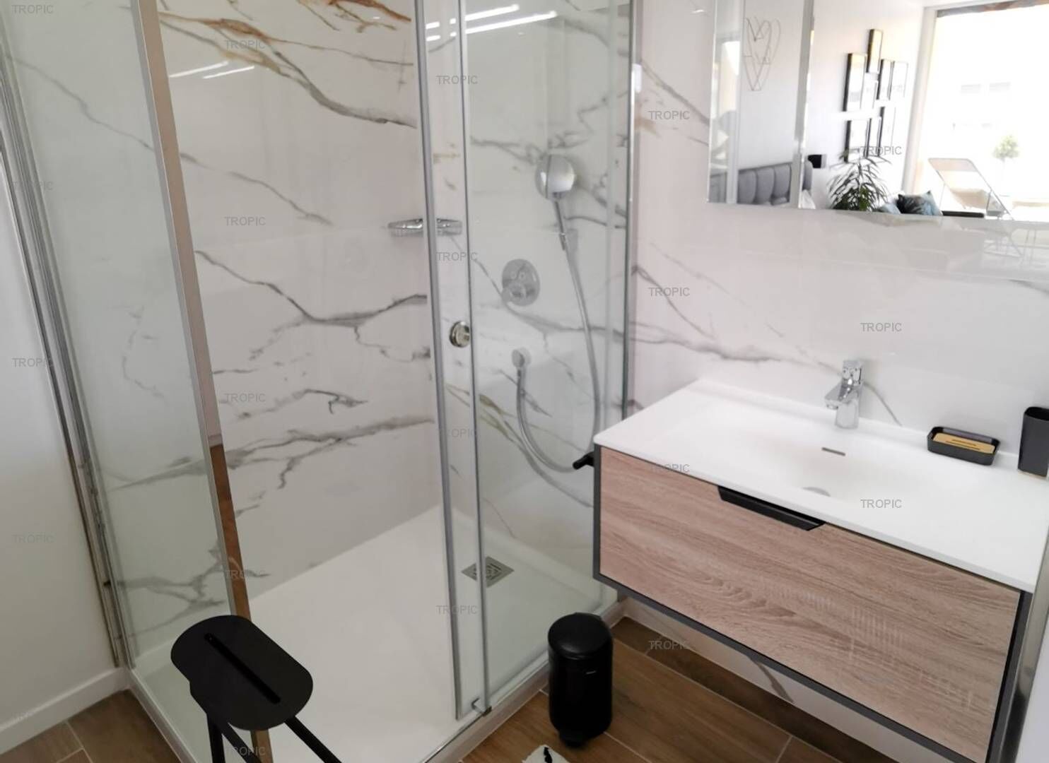 A modern bathroom with a glass shower enclosure, a white sink with a wooden cabinet, and a mirror above the sink.