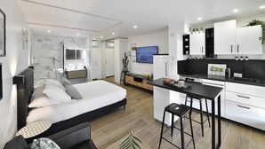 Quarto de hotel moderno com cama, um espaço de estar pequeno, cozinha compacta e banheiro.