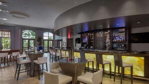 Zona de bar moderna con una barra curva, taburetes y un área de estar con mesas redondas y sillas.