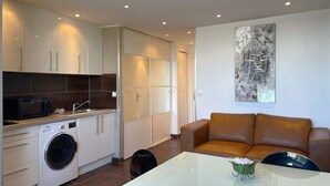 A modern kitchen with a washing machine, a dining table with chairs, and a brown leather sofa. - BROWN - Studio Héliopolis D 29 - Luxury - 2 people (AGDE)
