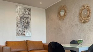 A modern living room with a brown leather sofa, a glass coffee table, and a dining area with a white table and black chairs. - BROWN - Studio Héliopolis D 29 - Luxury - 2 people (AGDE)