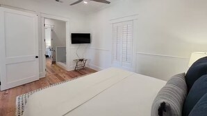 Ein Schlafzimmer mit einem Bett, einem Deckenventilator, einem an der Wand befestigten Fernseher und einem Fenster mit Rollläden.