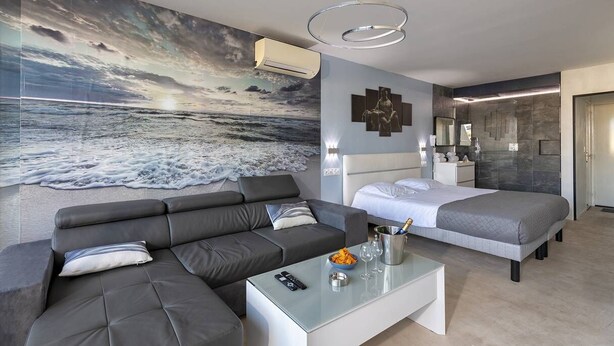 Una moderna camera d'albergo con un grande murale a tema oceano, un divano, un letto, un tavolino da caffè in vetro e un mini-frigorifero.