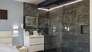 Una camera d'albergo moderna con un letto, una toeletta con specchio, una doccia con porta in vetro e un lampadario a parete.