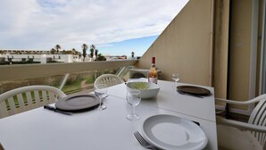 A table set for two on a balcony with a clear view of the ocean and palm trees in the background. - Studio Héliopolis D 51 - 4 people (AGDE)